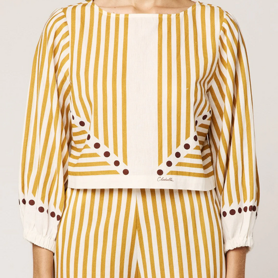 Woman wearing a yellow and white striped outfit with polka dot details on a plain background
