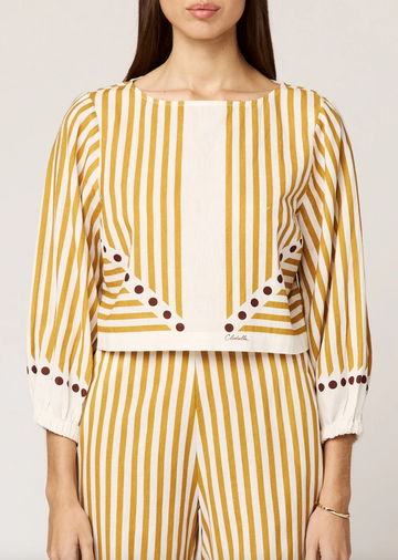 Woman wearing a yellow and white striped outfit with polka dot details on a plain background