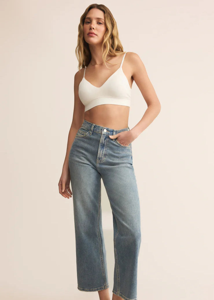 Woman wearing a white crop top and blue jeans on a beige background