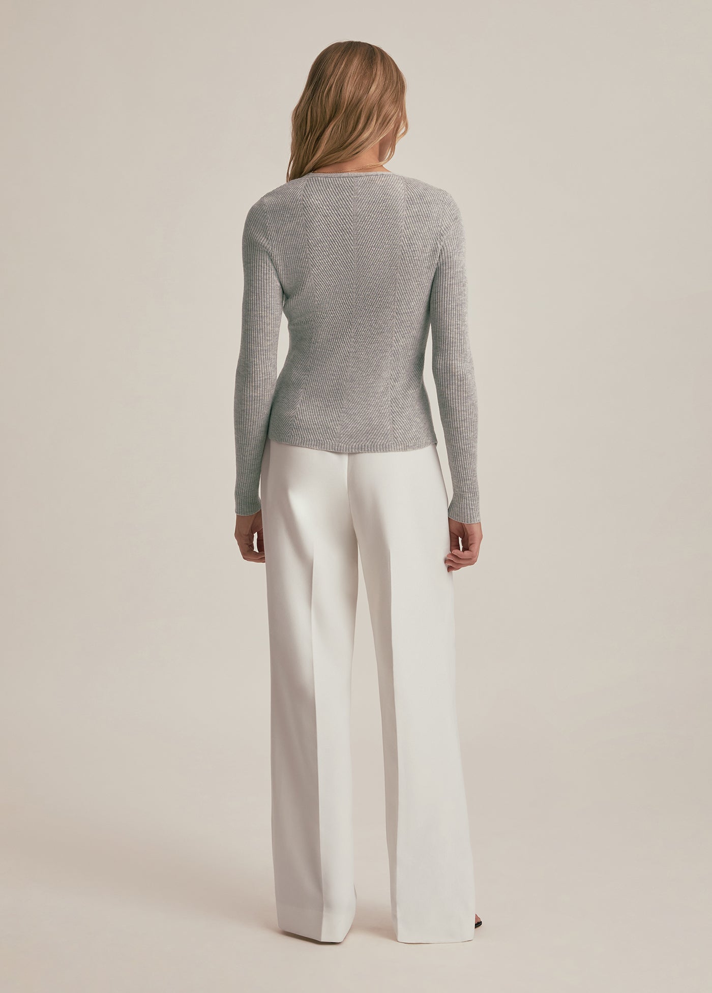 Woman wearing a gray sweater and white pants on a beige background