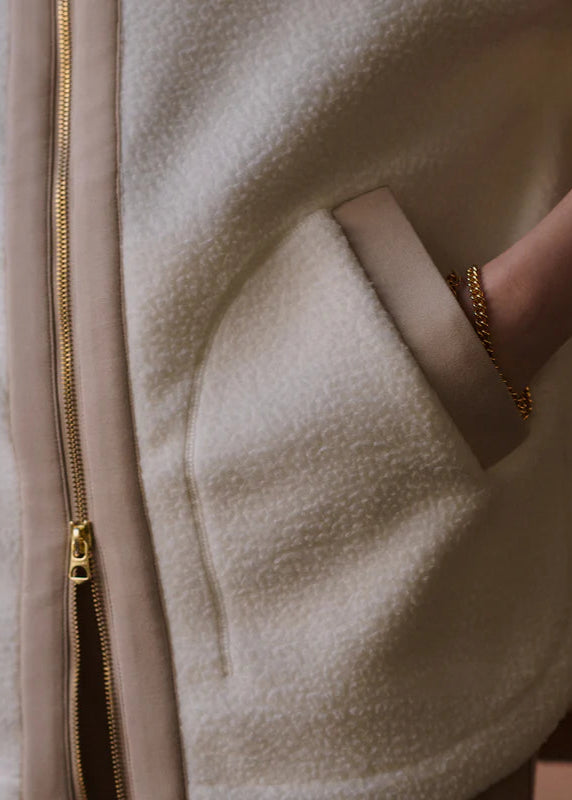 Close-up of a beige fleece jacket with a gold zipper and a hand wearing a gold ring.