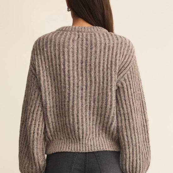 Person wearing a chunky knit sweater from behind on a beige background