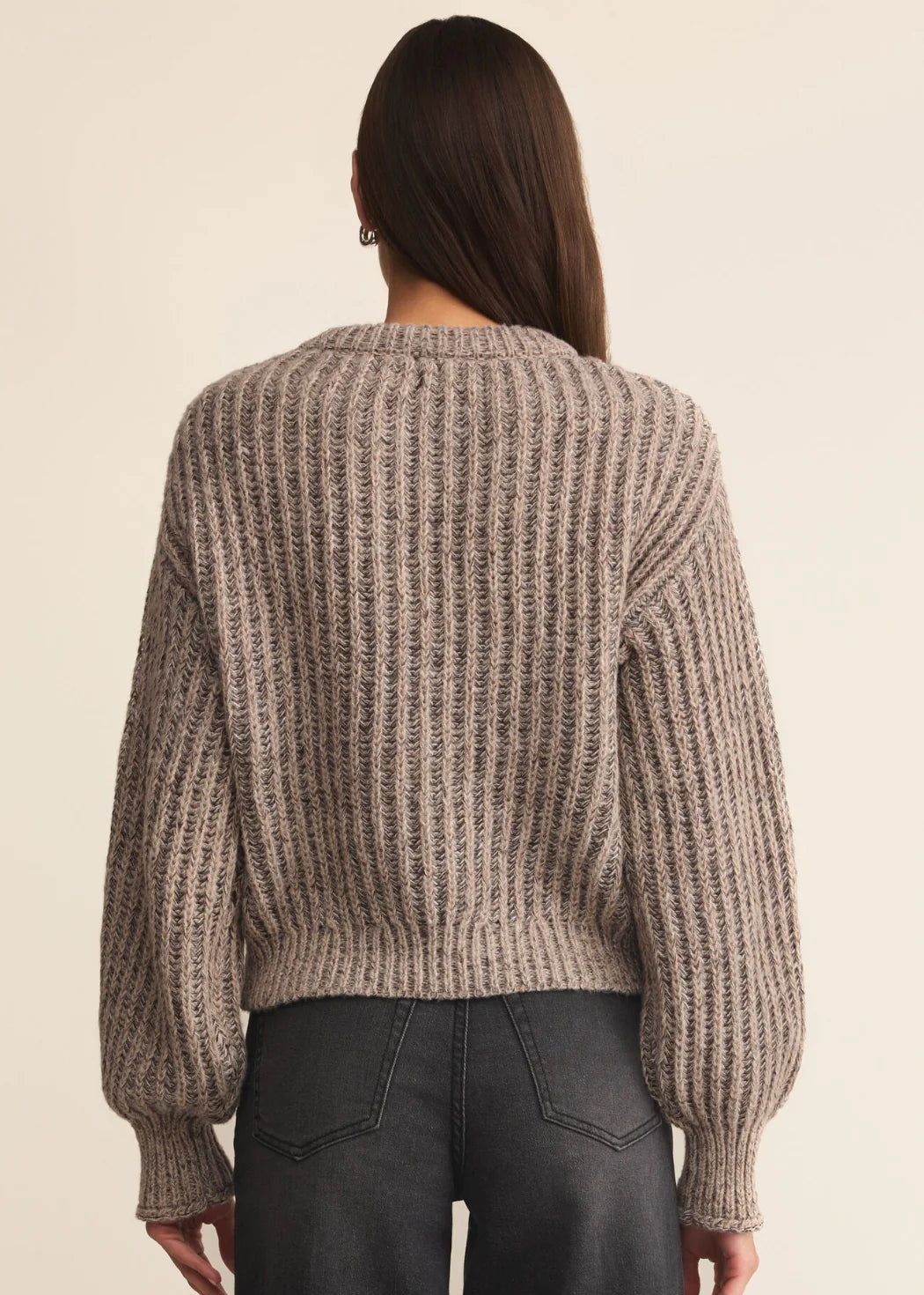 Person wearing a chunky knit sweater from behind on a beige background