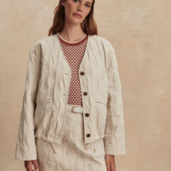 Woman wearing a beige quilted jacket and skirt set against a beige background