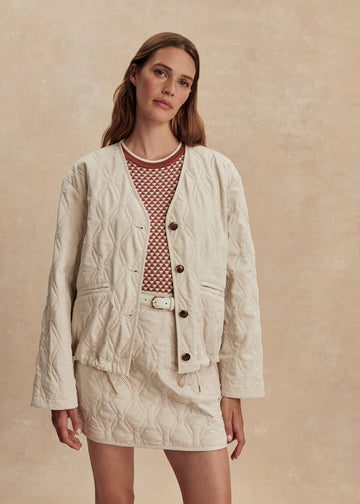 Woman wearing a beige quilted jacket and skirt set against a beige background