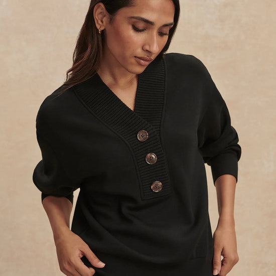 Woman wearing a black sweater with buttons on a beige background