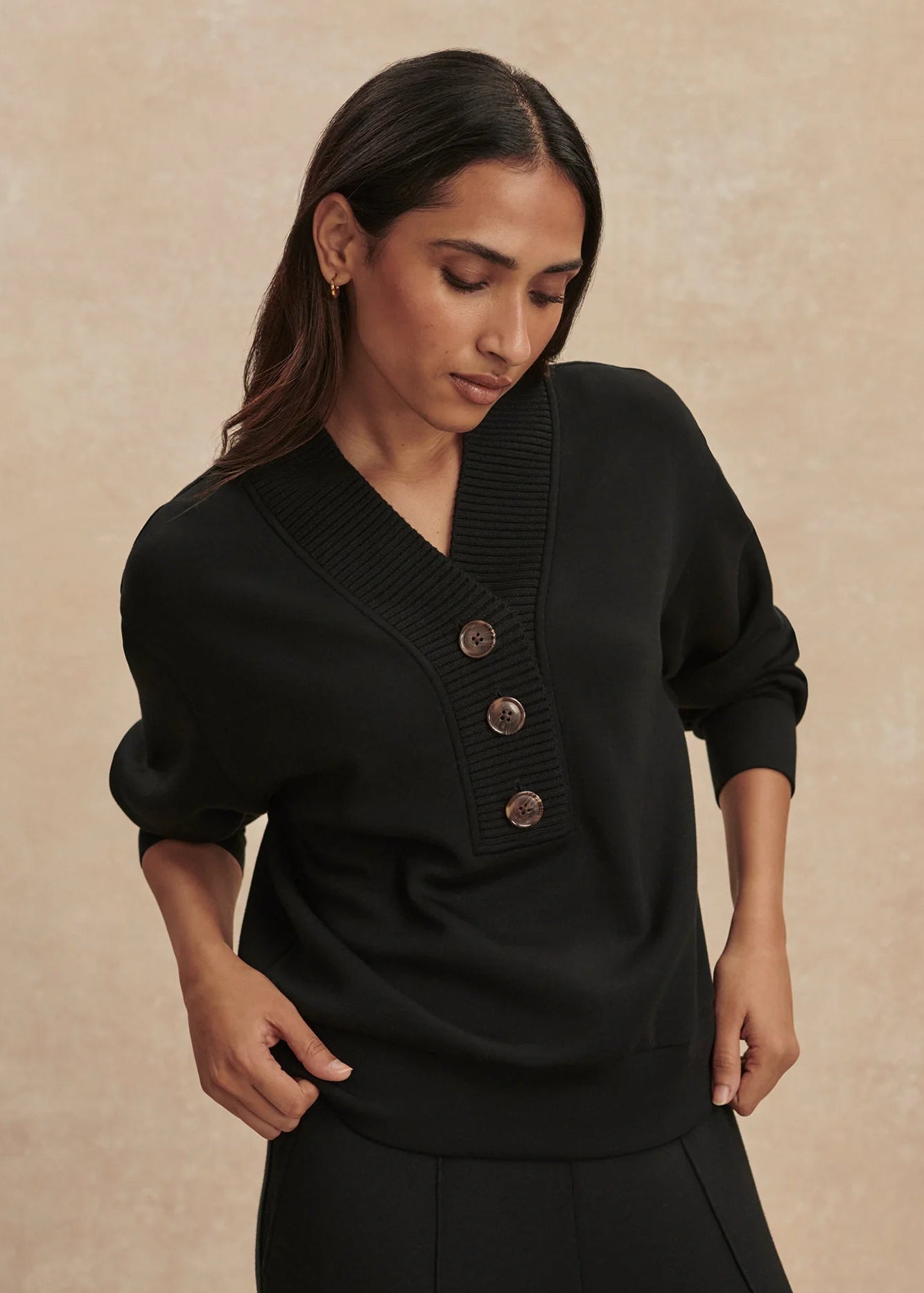 Woman wearing a black sweater with buttons on a beige background