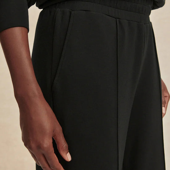 Close-up of a person wearing black pants with a neutral background