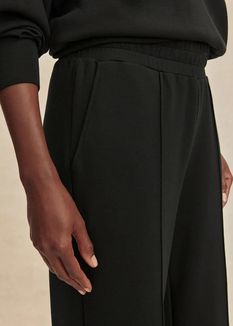 Close-up of a person wearing black pants with a neutral background