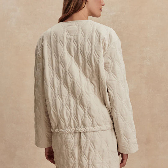 Woman wearing a beige quilted jacket and skirt set on a beige background