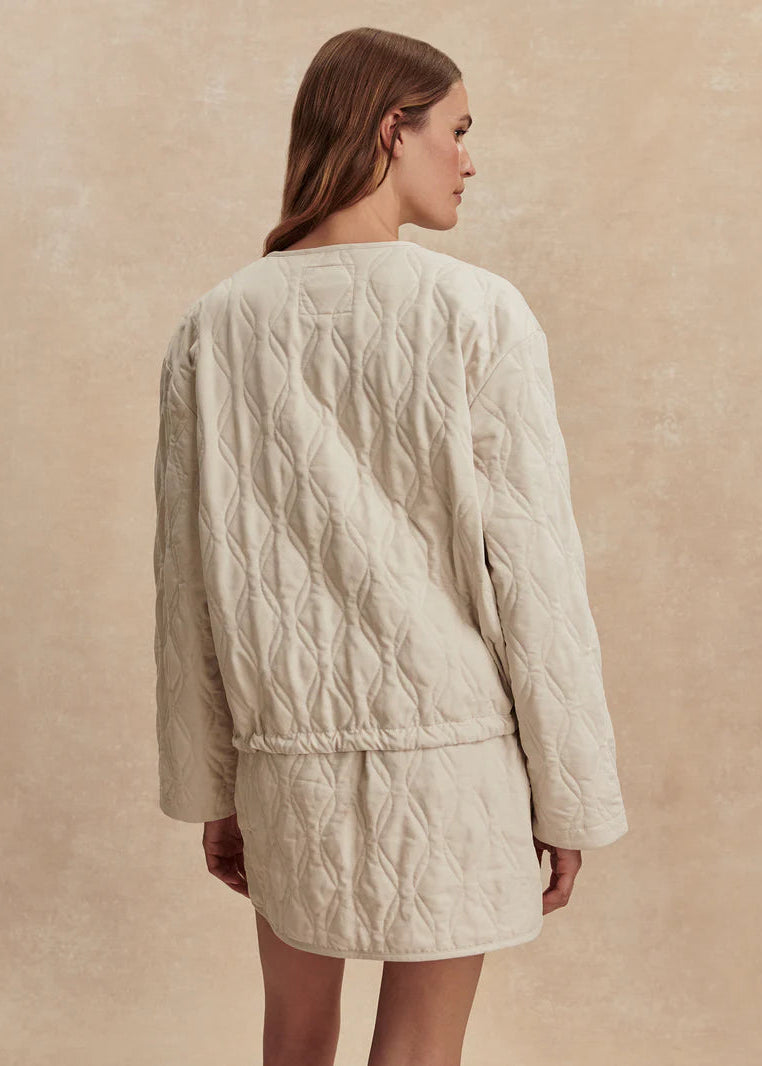 Woman wearing a beige quilted jacket and skirt set on a beige background