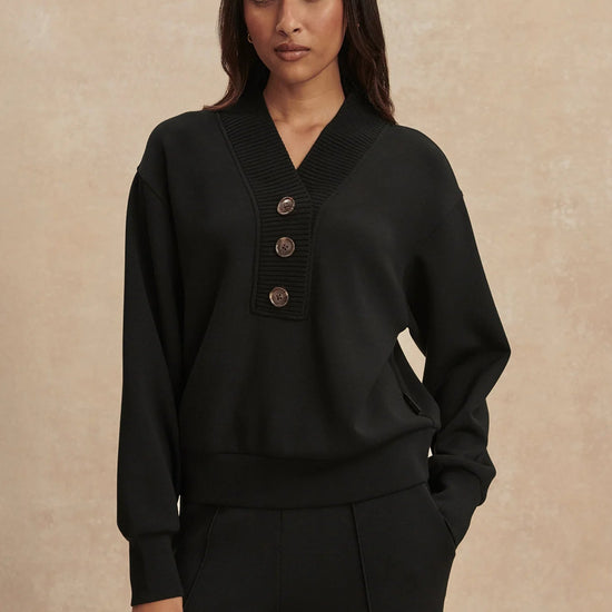 Woman wearing a black sweater with button details against a beige background