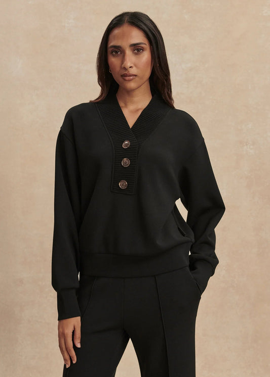 Woman wearing a black sweater with button details against a beige background