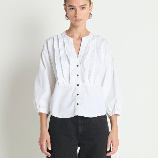 Person wearing a white blouse with black pants on a plain background