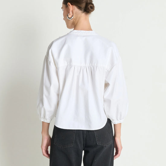 Person wearing a white blouse and black pants on a plain background