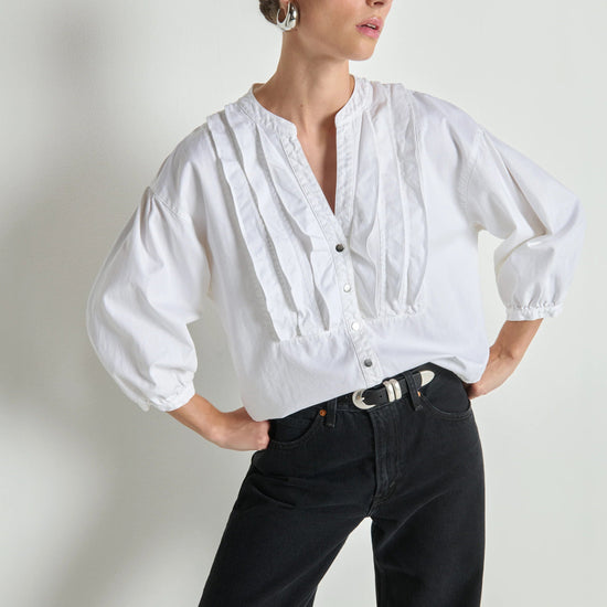 Woman wearing a white blouse and black pants against a plain background