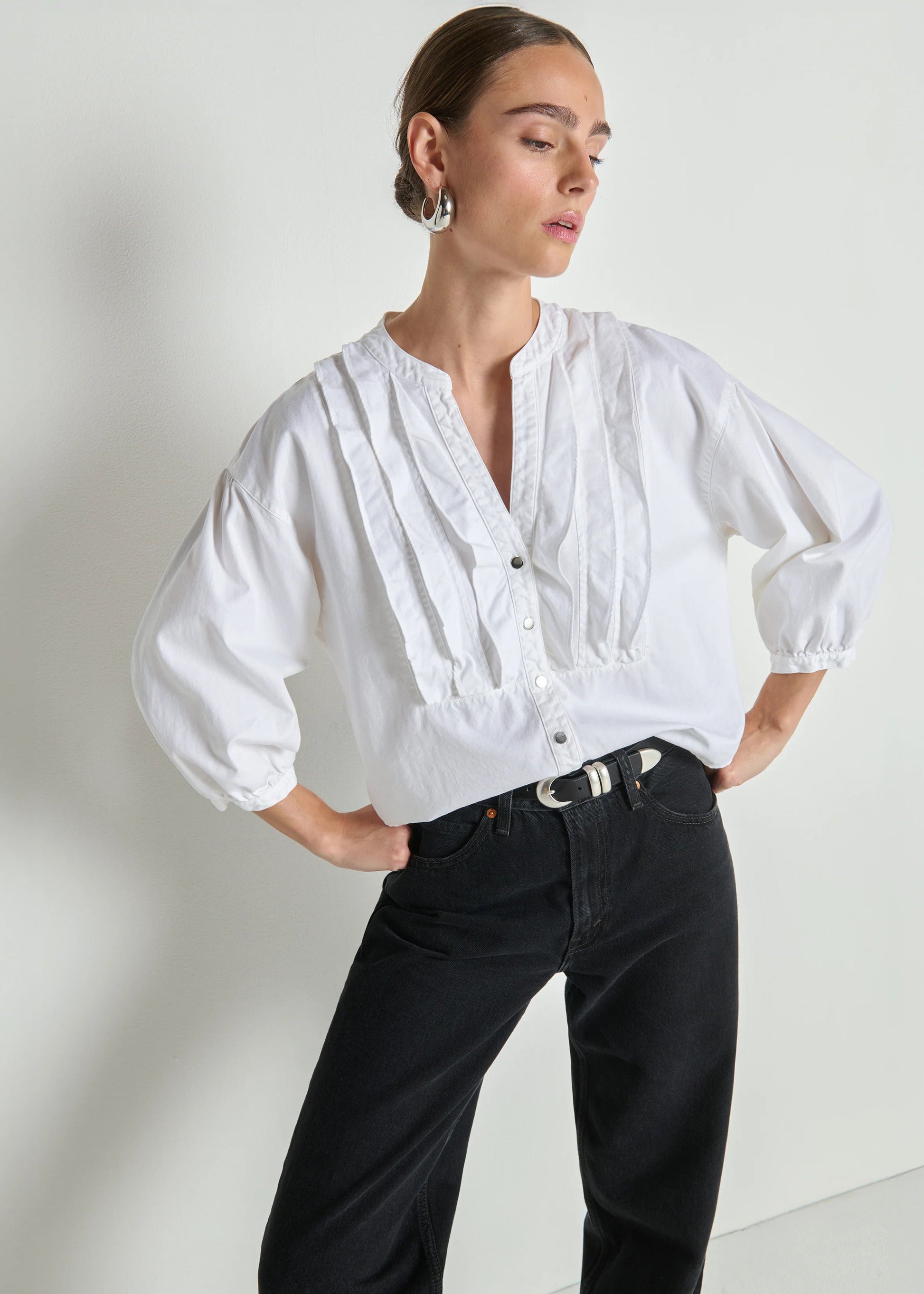 Woman wearing a white blouse and black pants against a plain background