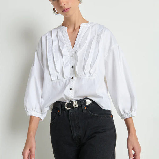 Woman wearing a white blouse with puffed sleeves and black pants on a plain background