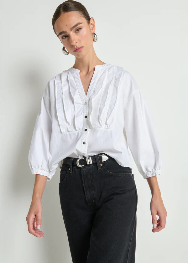 Woman wearing a white blouse with puffed sleeves and black pants on a plain background