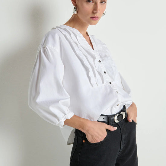 Woman wearing a white blouse and black pants against a plain background