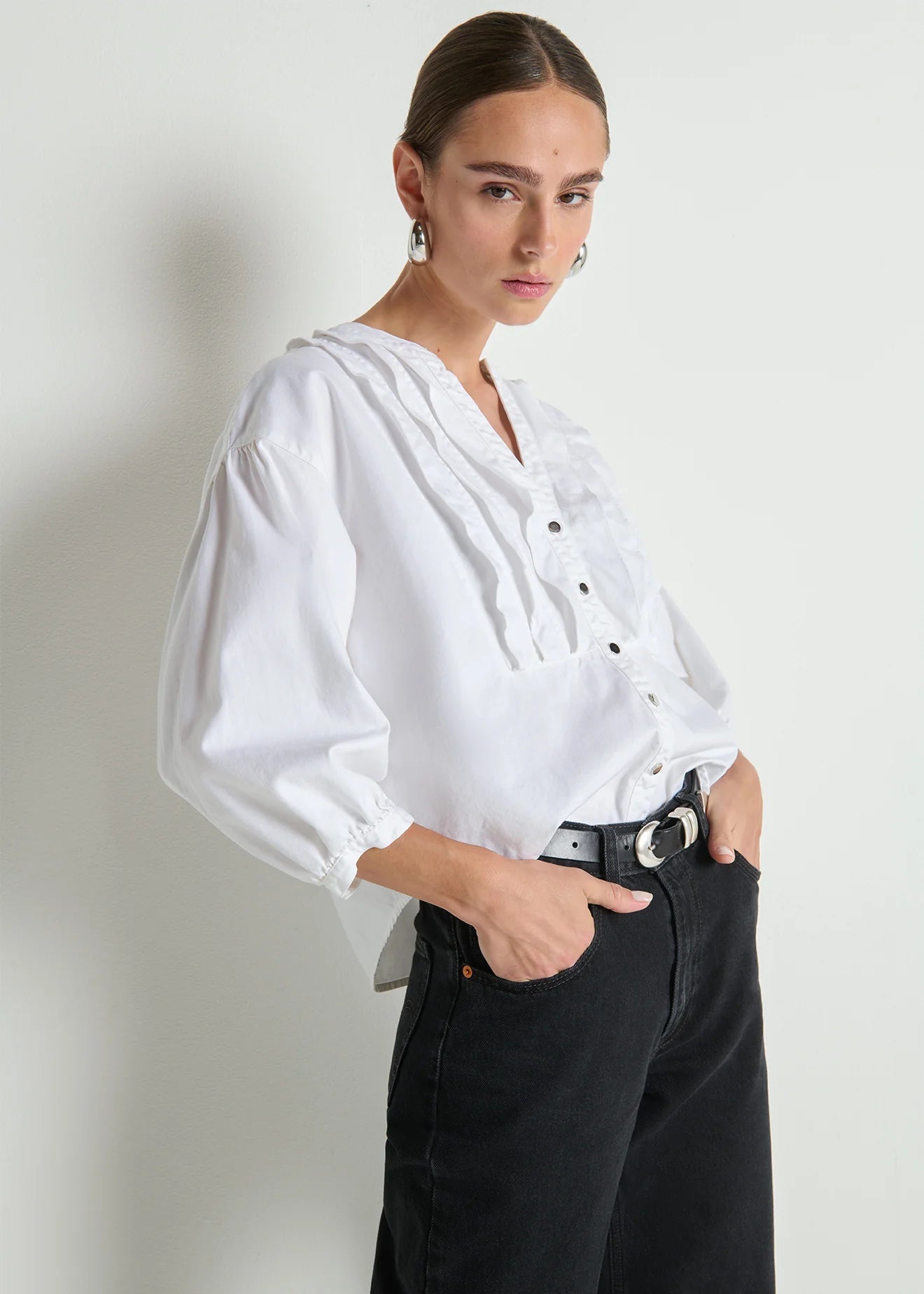 Woman wearing a white blouse and black pants against a plain background
