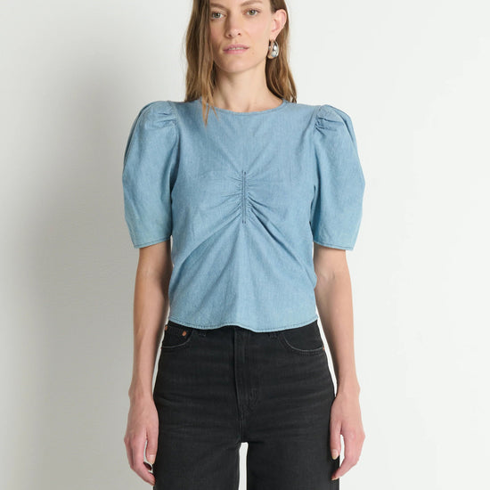 Woman wearing a light blue blouse with puff sleeves against a plain background