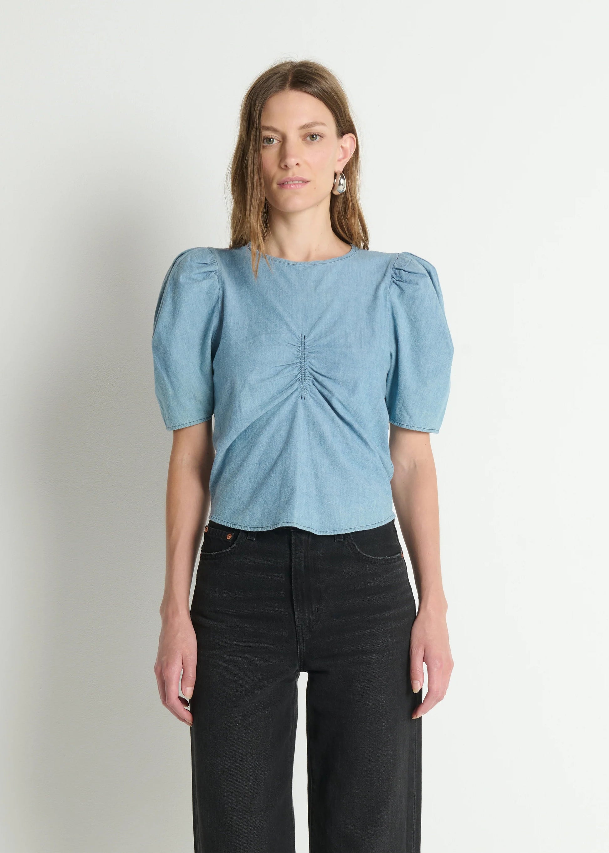 Woman wearing a light blue blouse with puff sleeves against a plain background