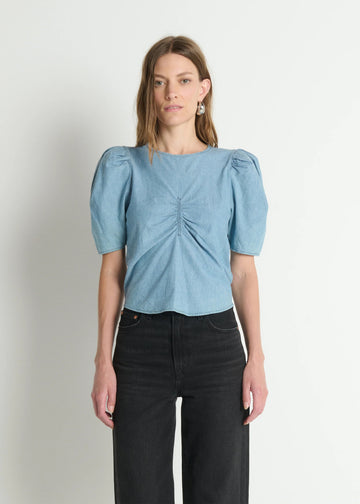 Woman wearing a light blue blouse with puff sleeves against a plain background