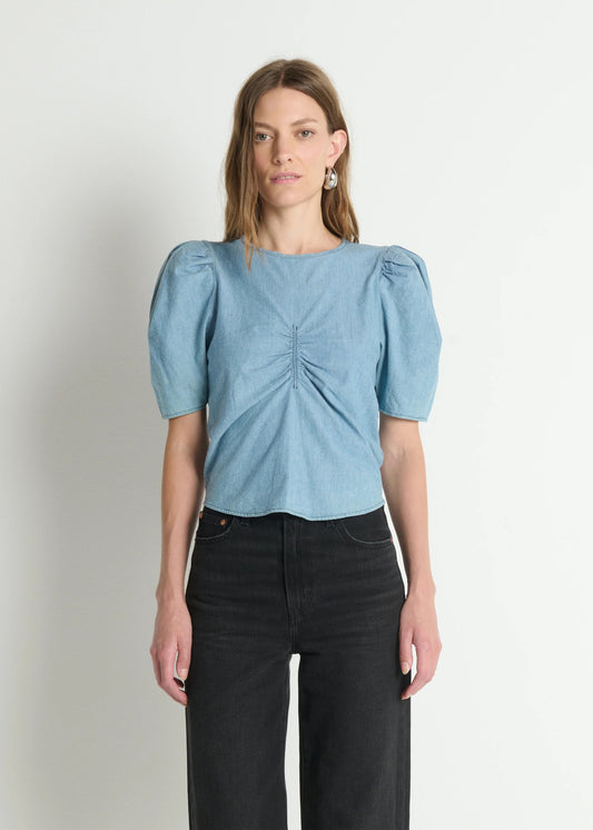 Woman wearing a light blue blouse with puff sleeves against a plain background