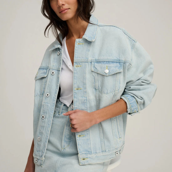 Woman wearing a light blue denim jacket and skirt on a plain background