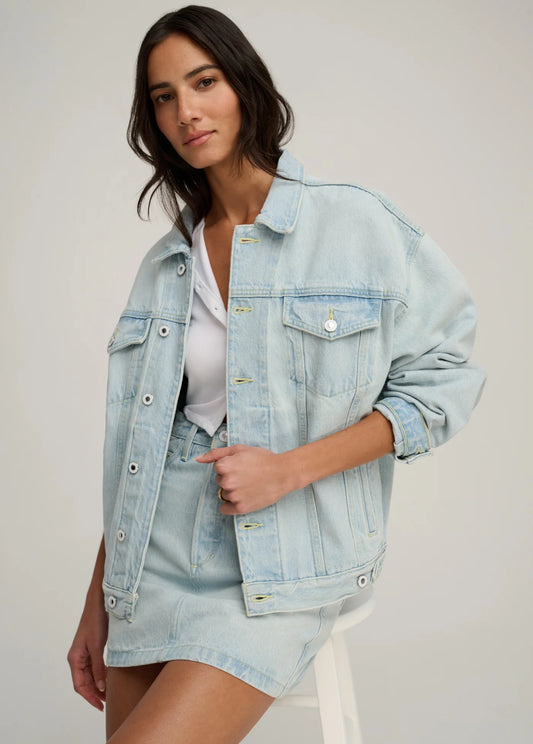 Woman wearing a light blue denim jacket and skirt on a plain background