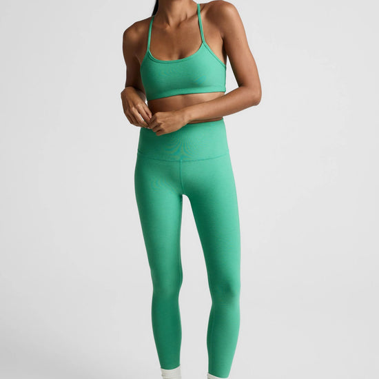 Woman wearing a green sports bra and leggings set on a light gray background