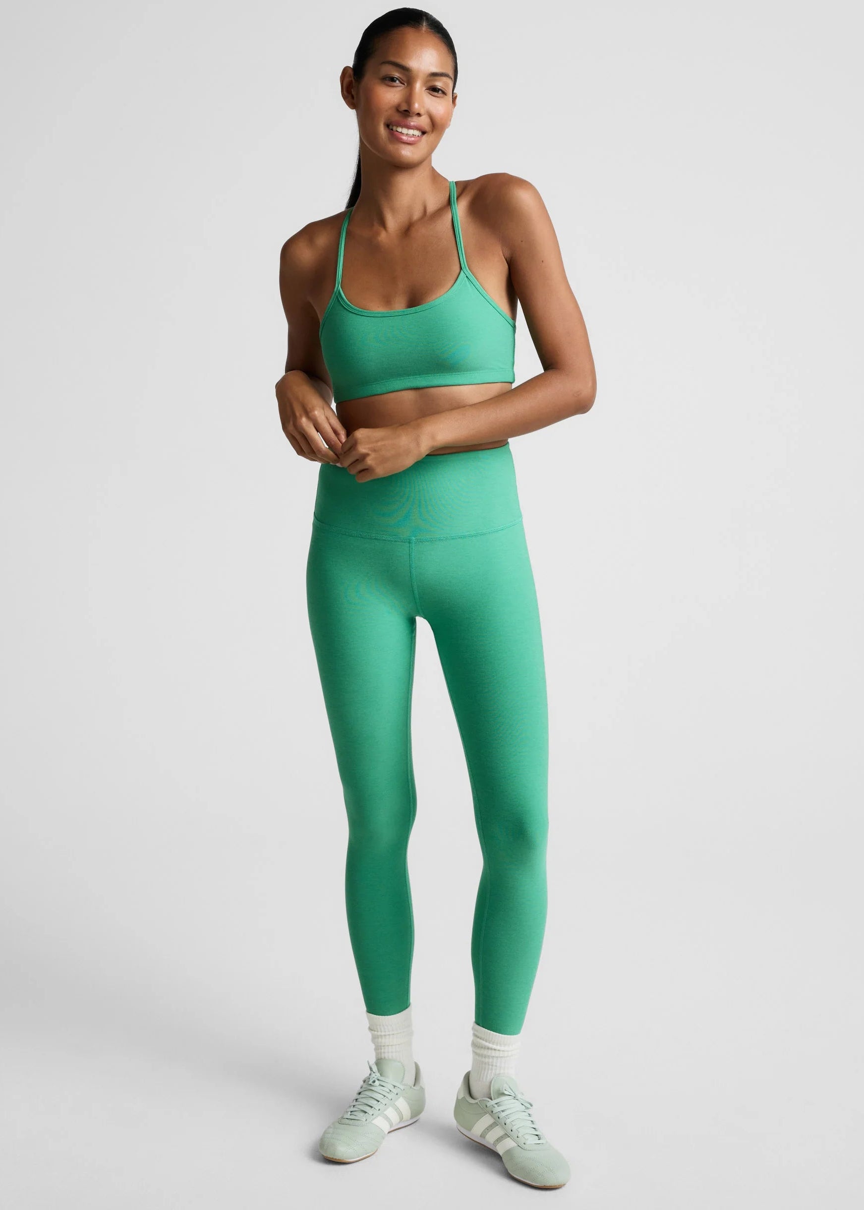 Woman wearing a green sports bra and leggings set on a light gray background