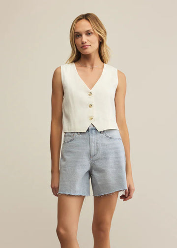 Woman wearing a white sleeveless top and light blue shorts on a beige background