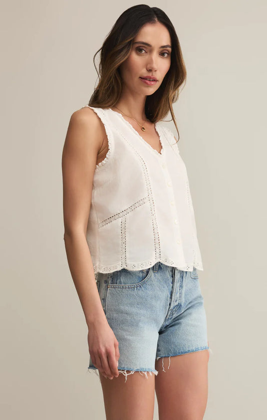 Woman wearing a white sleeveless top and denim shorts on a plain background