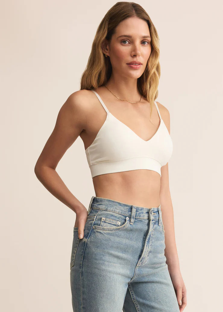 Woman wearing a white crop top and blue jeans against a beige background
