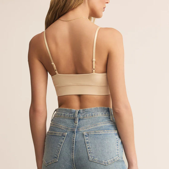 Woman wearing a beige crop top and blue jeans on a beige background