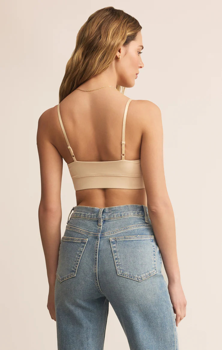 Woman wearing a beige crop top and blue jeans on a beige background