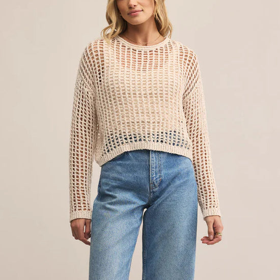 Woman wearing a beige knitted sweater and blue jeans on a beige background