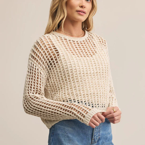Woman wearing a beige mesh sweater and blue jeans on a plain background