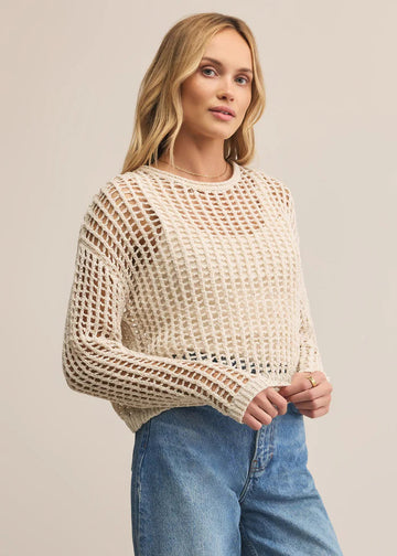 Woman wearing a beige mesh sweater and blue jeans on a plain background