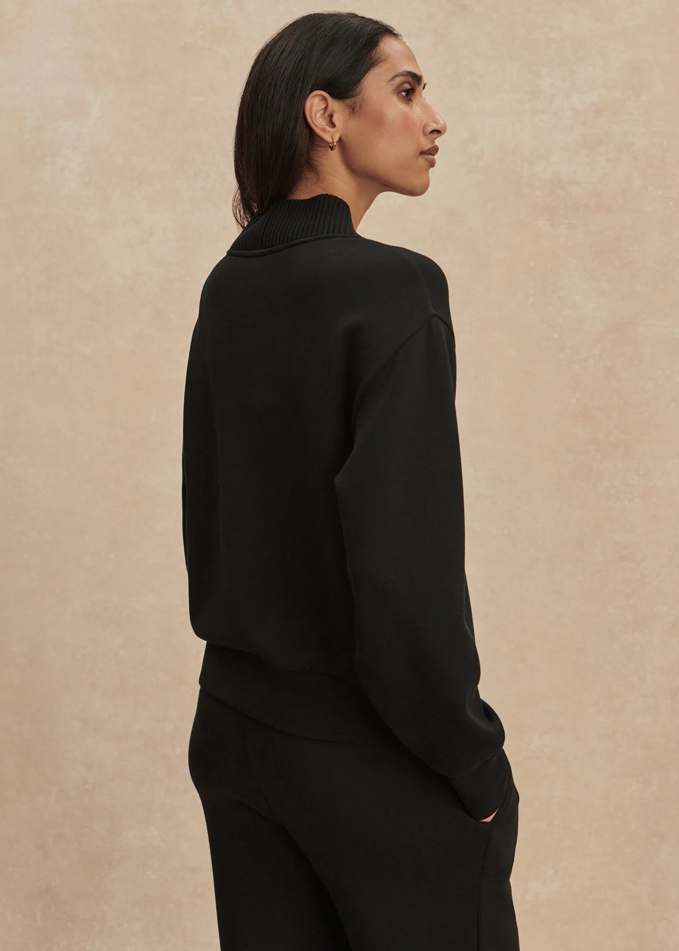 Woman wearing a black turtleneck sweater against a beige background