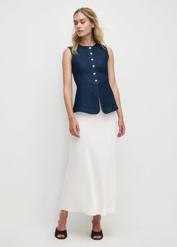 Woman wearing a dark denim vest over a white dress on a white background