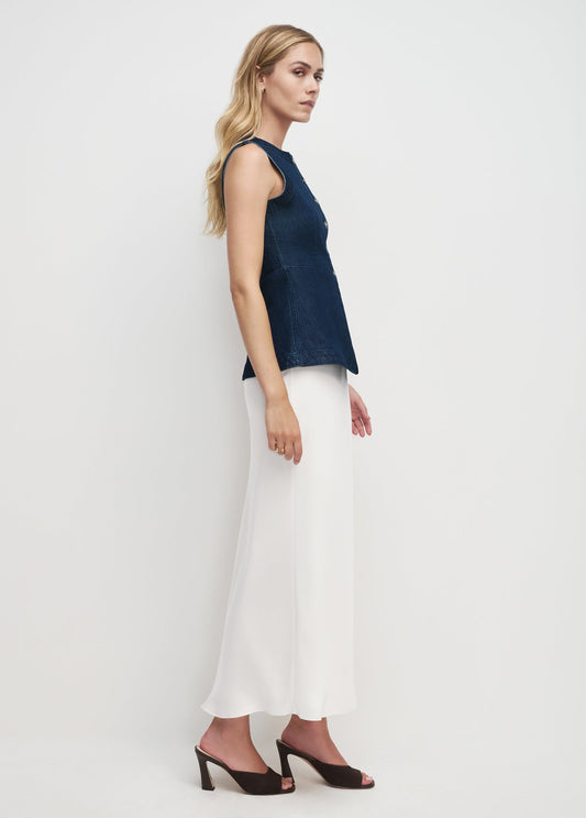 Woman wearing a dark blue sleeveless top and white pants on a light gray background