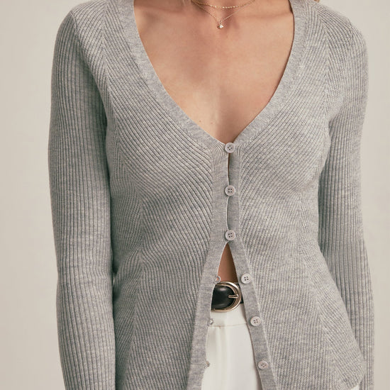 Woman wearing a gray ribbed cardigan over a black top with a beige background