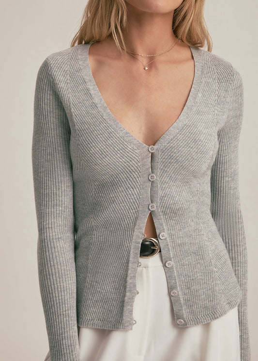 Woman wearing a gray ribbed cardigan over a black top with a beige background