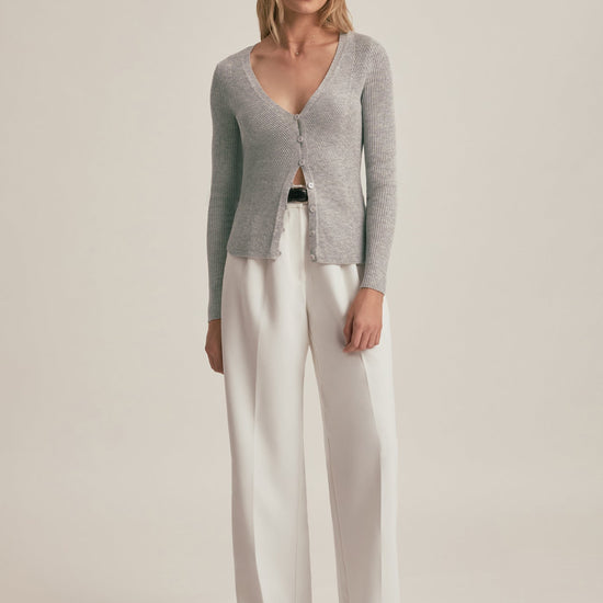 Woman wearing a gray cardigan and white pants on a beige background
