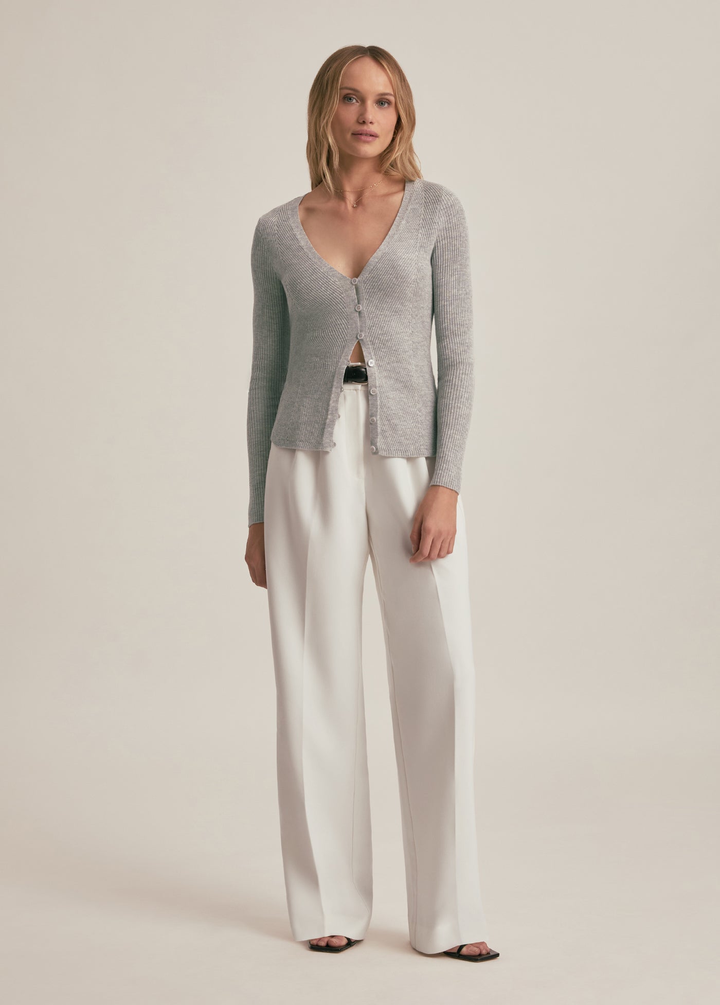 Woman wearing a gray cardigan and white pants on a beige background