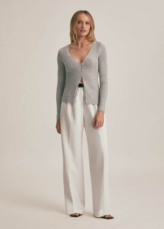 Woman wearing a gray cardigan and white pants on a beige background