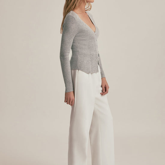 Woman wearing a gray sweater and white pants on a beige background